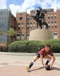 FSU Rugby player crouched in front of the Unconquered statue on campus